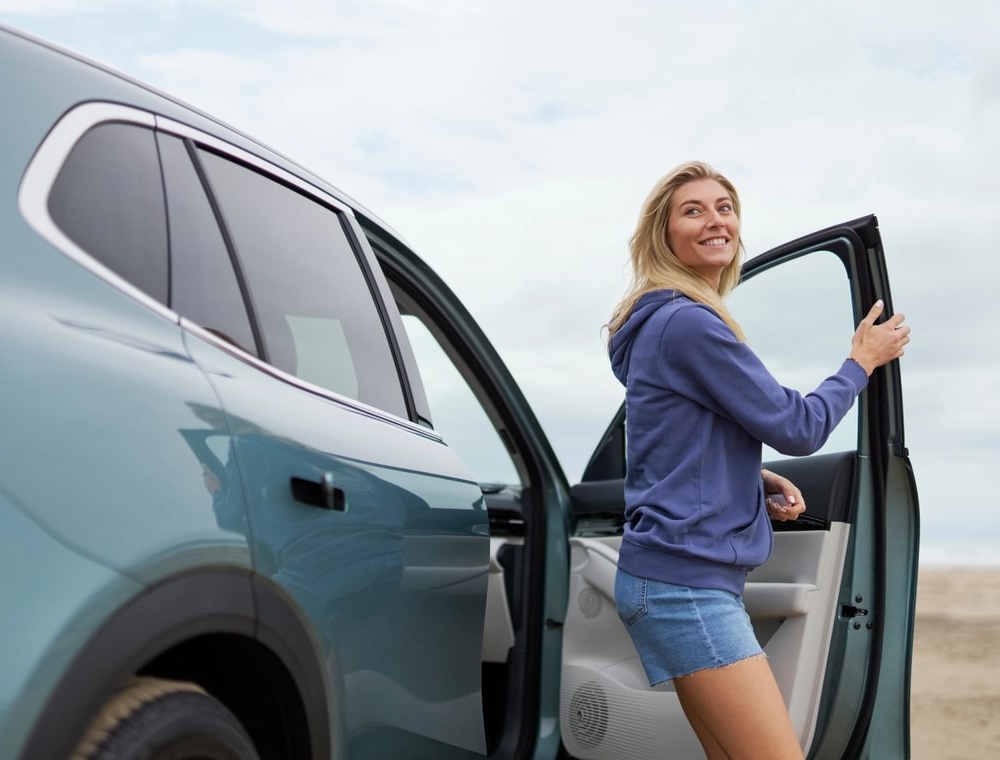 Woman opening the door of a Geely EX5 SUV by the coast.