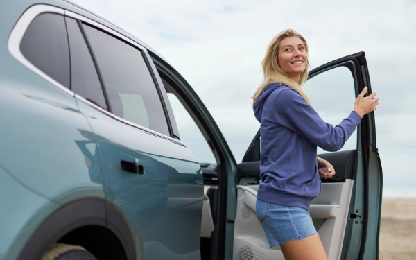 Woman opening the door of a Geely EX5 SUV by the coast.
