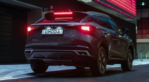 Rear shot of an OMODA 5 SHS-H, showing off the lit rear lighting and OMODA branding. The backdrop consists of modern buildings at night as the car is parked in the street.