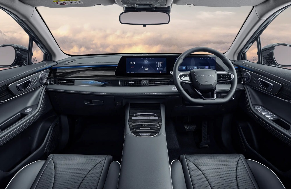 Interior of the new OMODA 5 SHS-H, showing off the driving position including the steering wheel and infotainment system. The background is fluffy clouds.