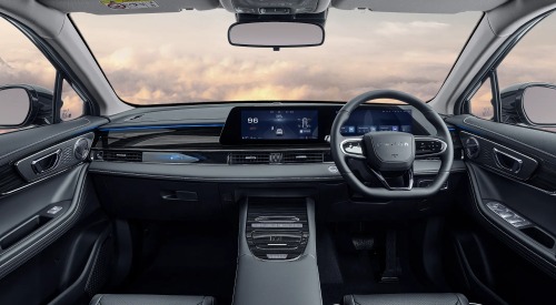Interior of the new OMODA 5 SHS-H, showing off the driving position including the steering wheel and infotainment system. The background is fluffy clouds.