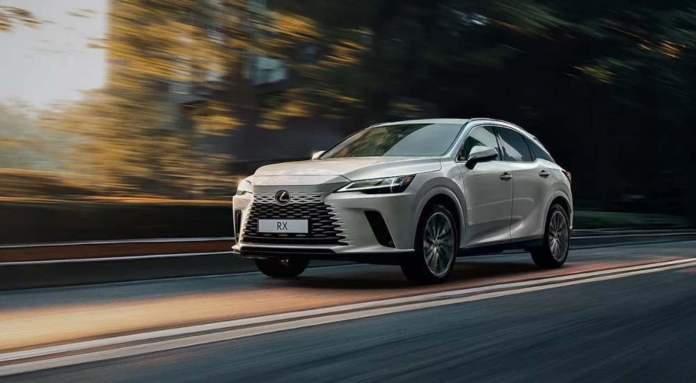 Lexus RX Self-Charging Hybrid in Pearlescent Sonic Titanium driving along a tree-lined road.