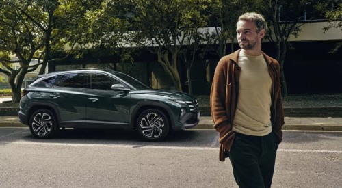 A person walking away from a parked Hyundai TUCSON Hybrid.