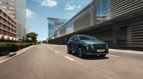 A new Hyundai TUCSON Hybrid driving down an empty city street at speed.