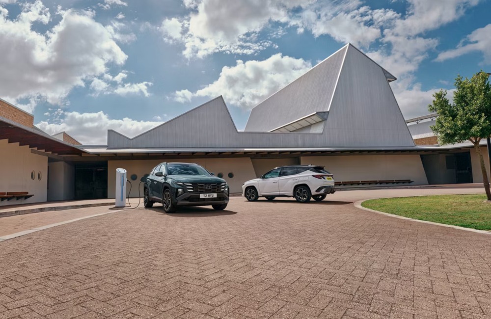 Two Hyundai TUCSON Plug-in Hybrid cars parked on a drive. One is plugged in and charging, showing off the front facade and grille, whilst the other is parked in away that shows the rear and side features.
