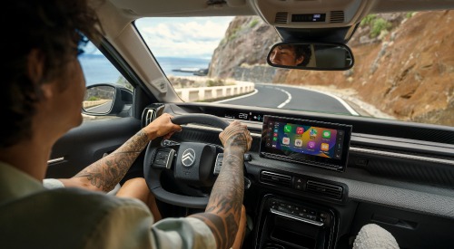 Interior shot of a person driving a new Citroen C3 Aircross down a coastal road at speed. The shot focusses on the person driving and shows off the infotainment system