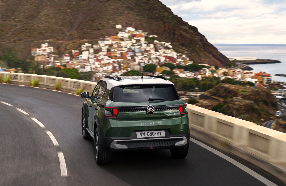Rear shot of a new Citroen C3 Aircross driving down a coastal road towards a cliff-side town. The car is moving at speed and showing off the rear design.