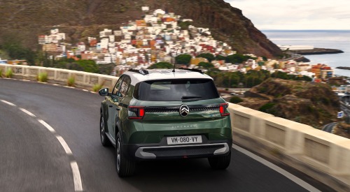 Rear shot of a new Citroen C3 Aircross driving down a coastal road towards a cliff-side town. The car is moving at speed and showing off the rear design.