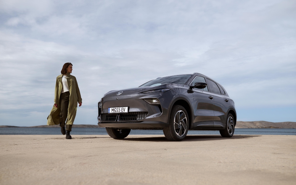 MGS5 EV in Camden Grey on sand with a woman walking beside it.