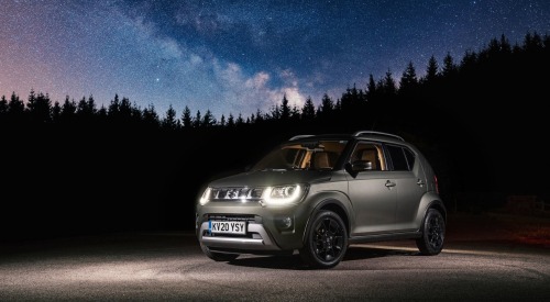 Angled shot of a Suzuki Ignis at night with a star-filled sky background. The car has its front headlights lit and is surrounded by dark forest, making it stand out with the night sky.