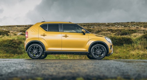 Side profile of a yellow Suzuki Ignis parked on a wet countryside road.