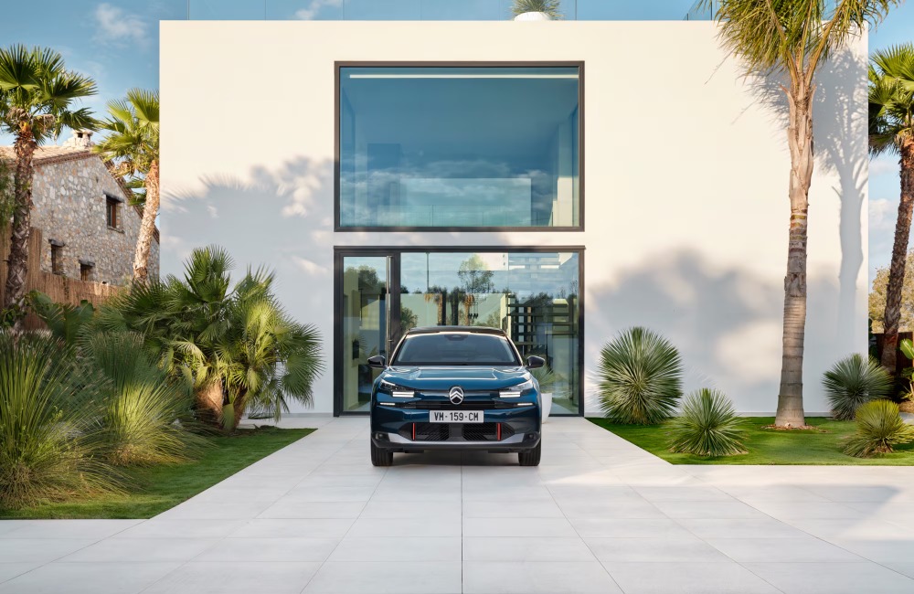 Front-facing shot of a new Citroen C4, the car is parked on the driveway of a modern white house in a tropical setting.