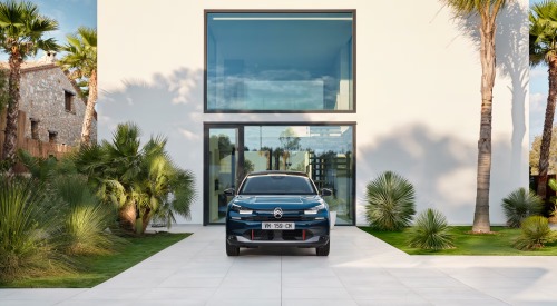 Front-facing shot of a new Citroen C4, the car is parked on the driveway of a modern white house in a tropical setting.