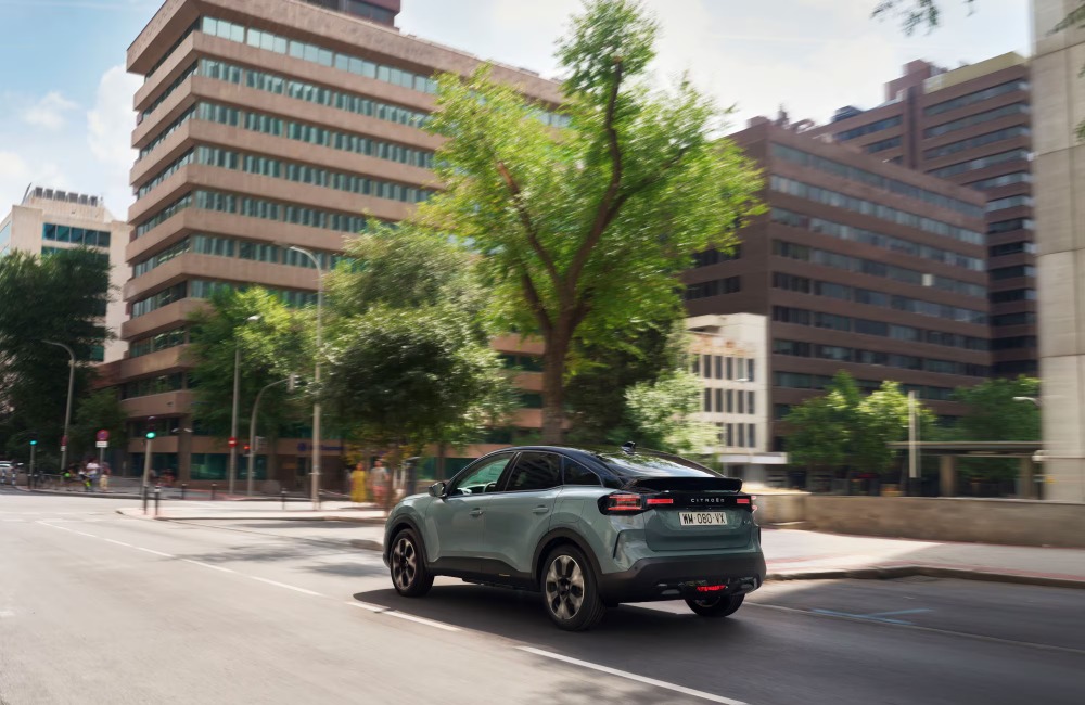 Rear shot of a new Citroen C4 driving down a city street on a sunny day.