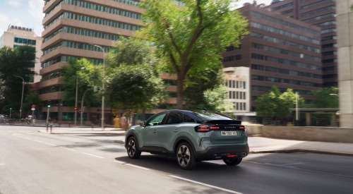 Rear shot of a new Citroen C4 driving down a city street on a sunny day.