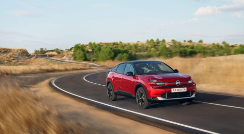 Citroen C4 driving at speed down a windy country-side road, surrounded by brown grass and green trees.