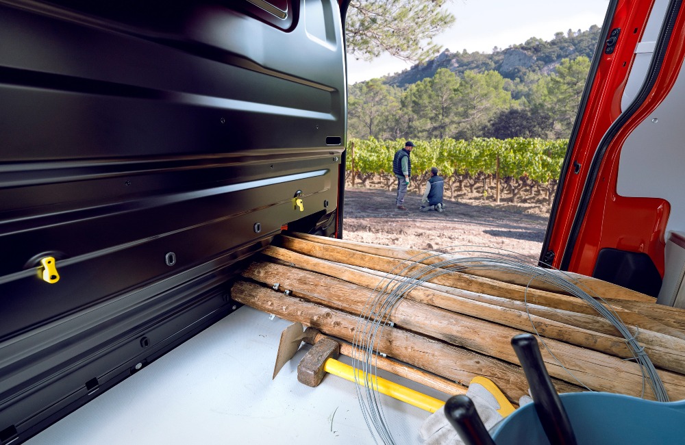 Interior shot of a used Citroen Dispatch van, showing off how it can hold long wooden objects. The owners are seen outside the van, prepping to build the fence with the materials inside the van.