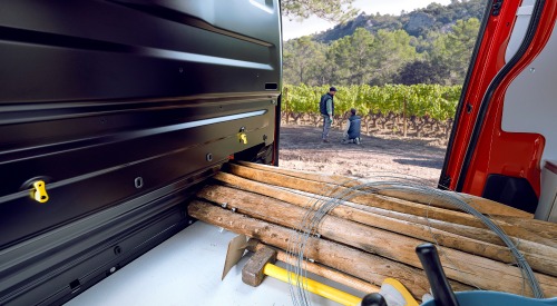 Interior shot of a used Citroen Dispatch van, showing off how it can hold long wooden objects. The owners are seen outside the van, prepping to build the fence with the materials inside the van.