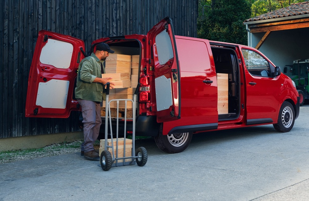 Person loading wooden blocks into the back of a used Citroen Dispatch. Both rear doors and the sliding side door are open, showing easy access to the wooden blocks.