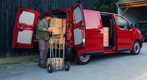 Person loading wooden blocks into the back of a used Citroen Dispatch. Both rear doors and the sliding side door are open, showing easy access to the wooden blocks.