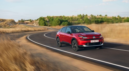 Red Citroen C4 driving at speed down an open road surrounded by brown grass and green trees.
