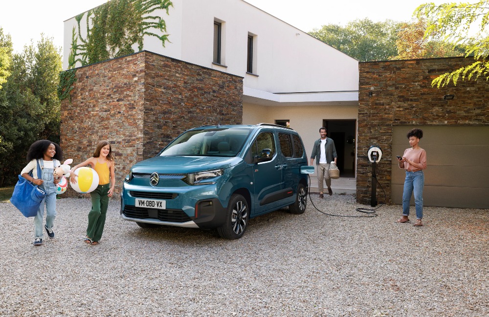 A family getting ready to go on away with beach gear. A Citroen e-Berlingo is parked and charging in front of their house.