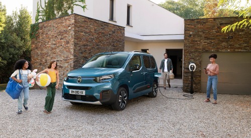 A family getting ready to go on away with beach gear. A Citroen e-Berlingo is parked and charging in front of their house.