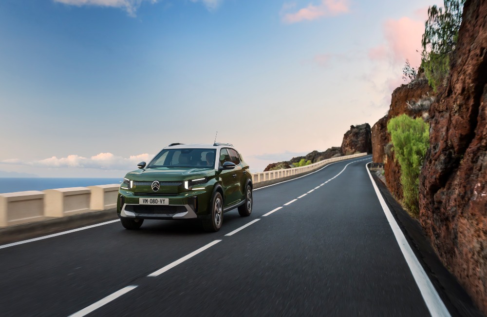 A green Citroen C3 Aircross driving at speed down a coastal cliff-side road.