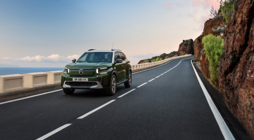 A green Citroen C3 Aircross driving at speed down a coastal cliff-side road.