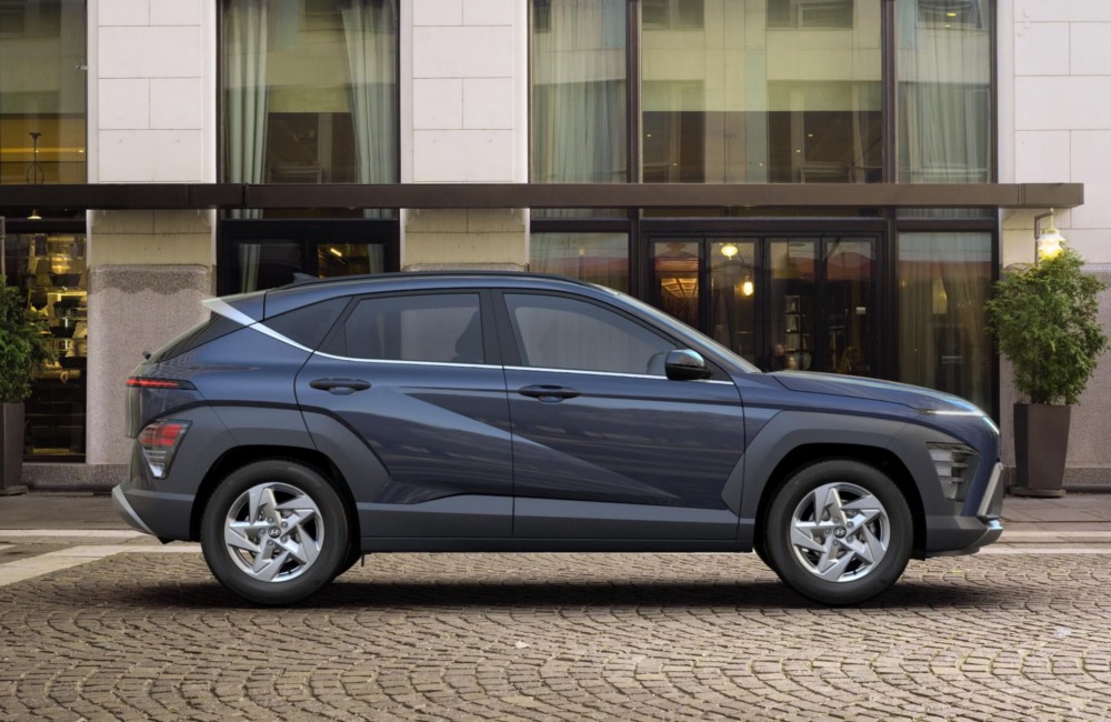 Side profile of a Hyundai KONA, parked on a cobbled road outside a modern building.