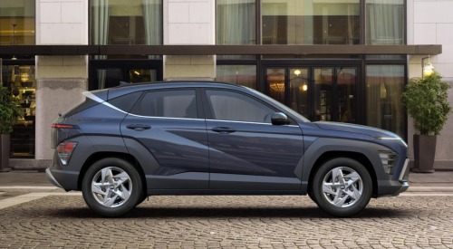 Side profile of a Hyundai KONA, parked on a cobbled road outside a modern building.