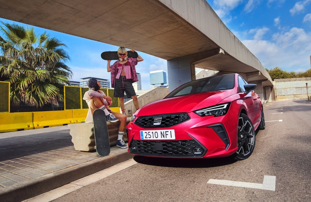 Two people with skateboards posing next to a new SEAT Ibiza which is parked on an urban street