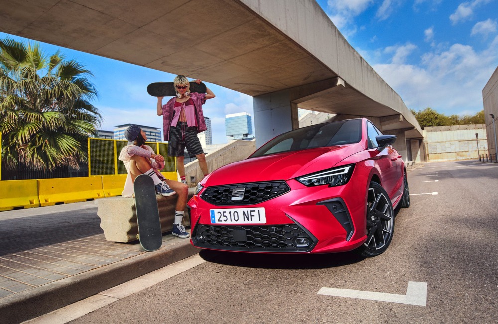 Two people with skateboards stood and sat down next to a SEAT Ibiza. The car is red and parked on the side of the road, showing off the LED lighting and unique look.