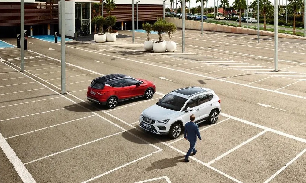 Two seat cars parked in an empty parking lot, a person is walking up to one, getting ready to get in.