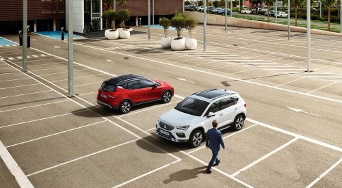 Two seat cars parked in an empty parking lot, a person is walking up to one, getting ready to get in.