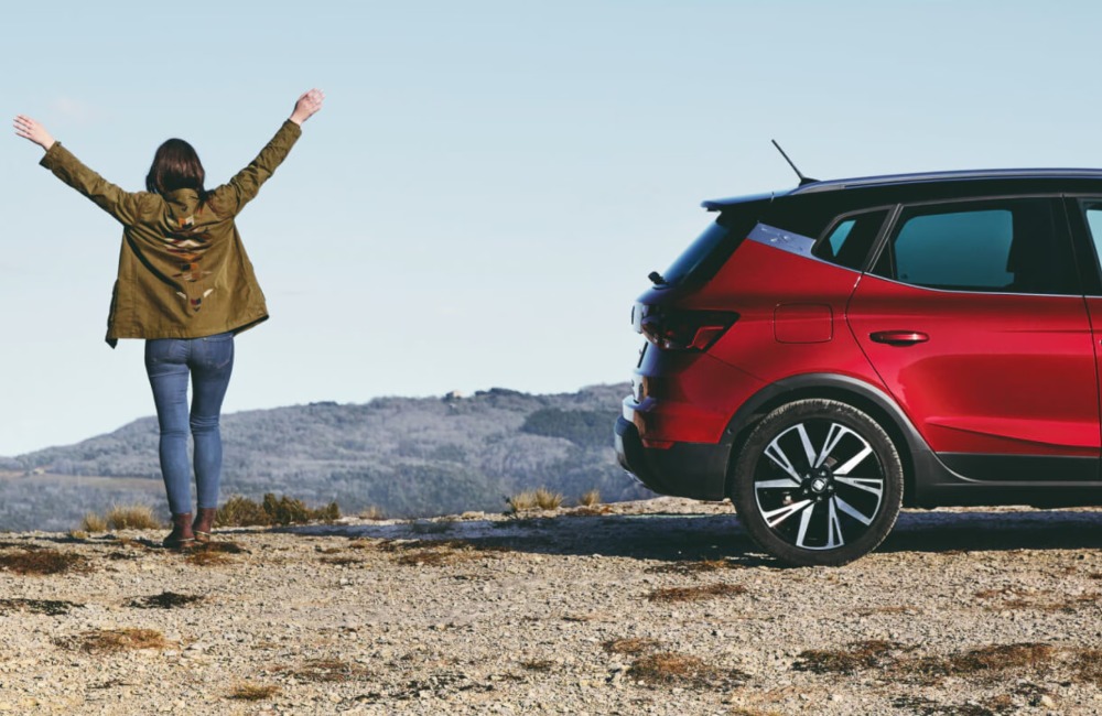 Persona stood next to a used SEAT car with their arms spread outward and to the side.