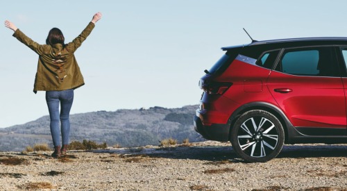 Persona stood next to a used SEAT car with their arms spread outward and to the side.
