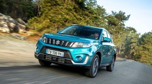 Angled front shot of a used Suzuki Vitara driving at speed down a country road surrounded by trees.