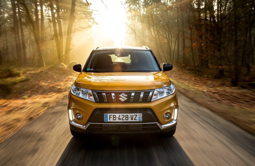 Front shot of a used Suzuki Vitara driving at speed down a forest road.