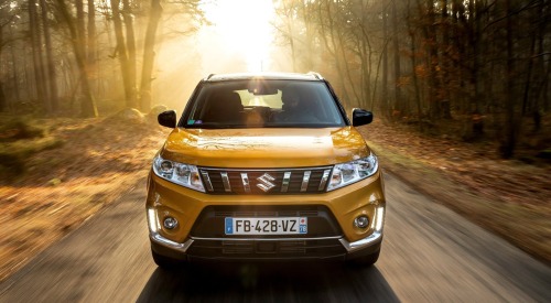 Front shot of a used Suzuki Vitara driving at speed down a forest road.