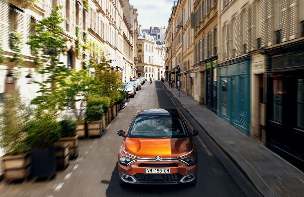 Front shot of a Citroen C4 driving down a narrow busy city street at speed.