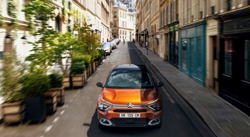 Front shot of a Citroen C4 driving down a narrow busy city street at speed.