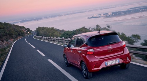Rear shot of a used Hyundai i10 driving at speed down a cliffside road.