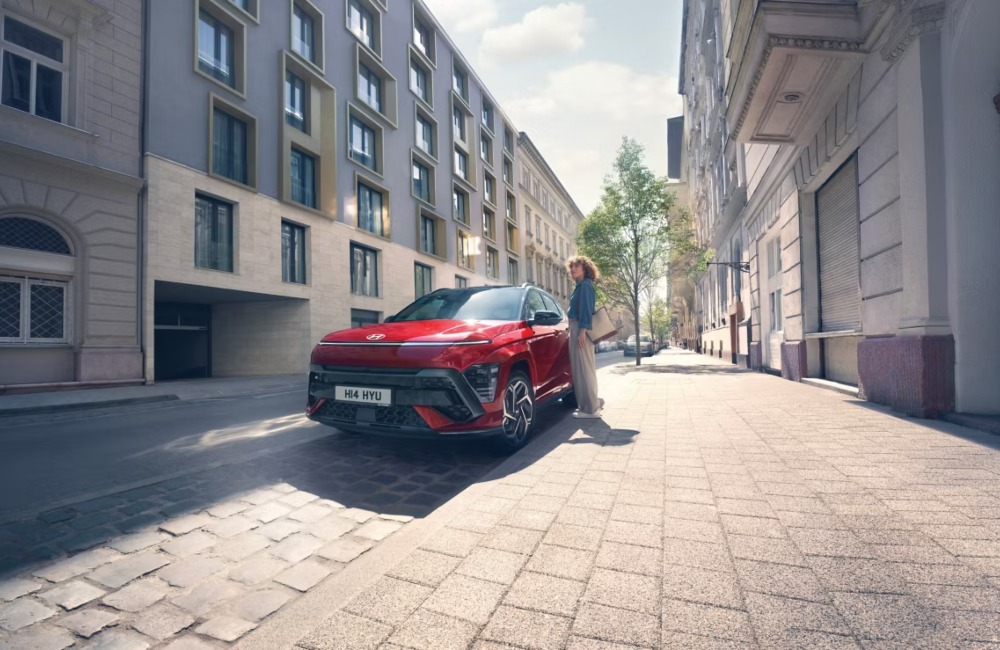 Person getting into a red Hyundai KONA that is parked on the side of a city street.