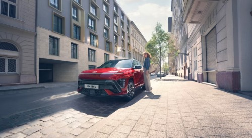 Person getting into a red Hyundai KONA that is parked on the side of a city street.