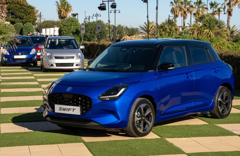 Multiple generations of Suzuki Swift cars parked next to one another in front of a modern version.