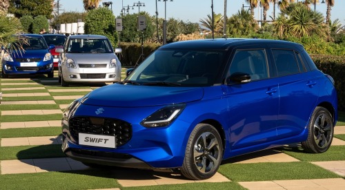 Multiple generations of Suzuki Swift cars parked next to one another in front of a modern version.