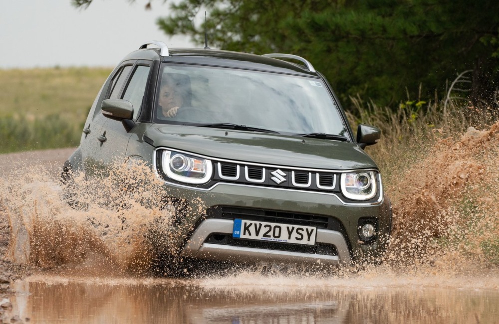 Suzuki Ignis driving through a large muddy puddle at speed, spraying muddy water.