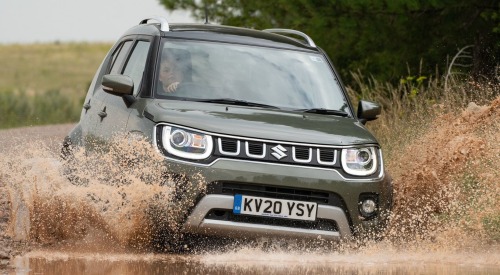 Suzuki Ignis driving through a large muddy puddle at speed, spraying muddy water.