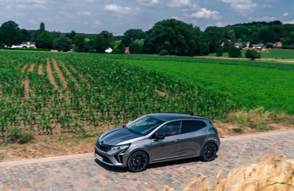 A used renault Clio driving on a cobbled road surrounded by fields of crops.